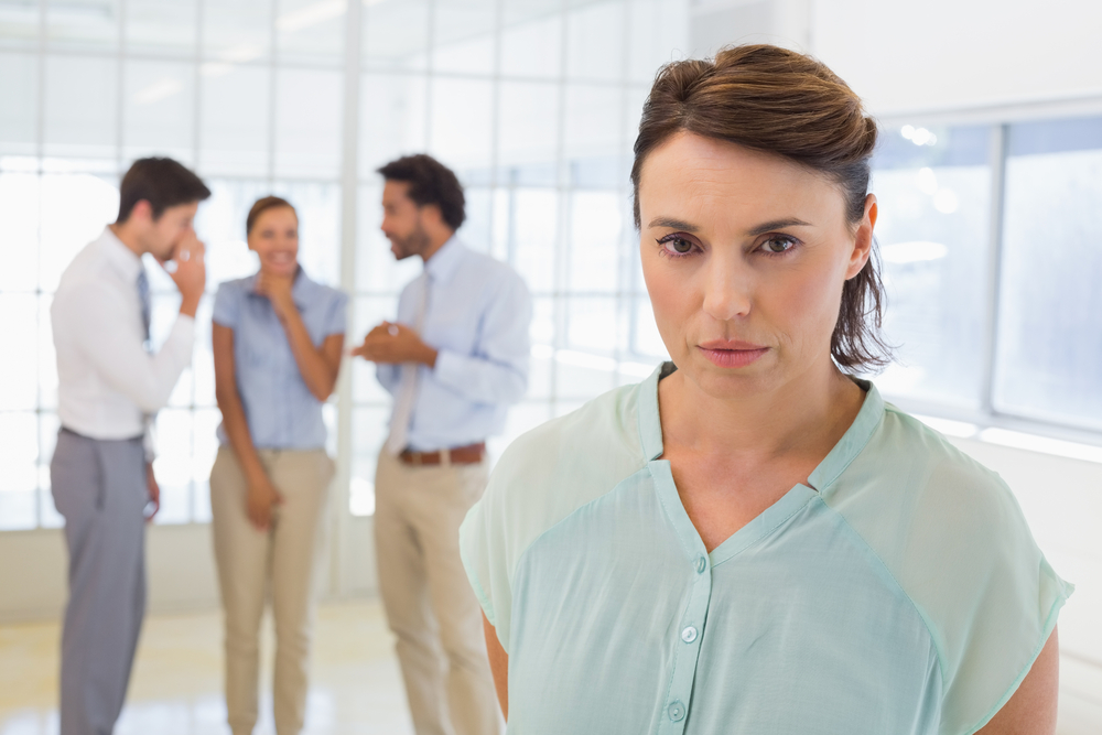 woman frowning with gossiping colleagues